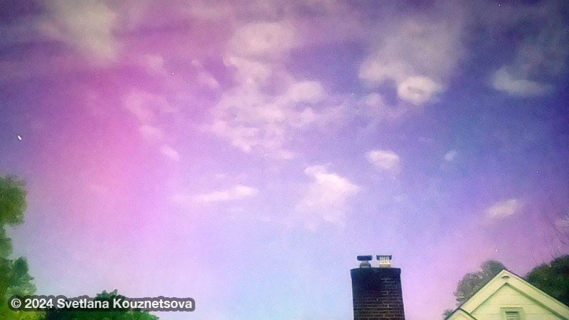Pink hues on the night sky with clouds above trees and a house.