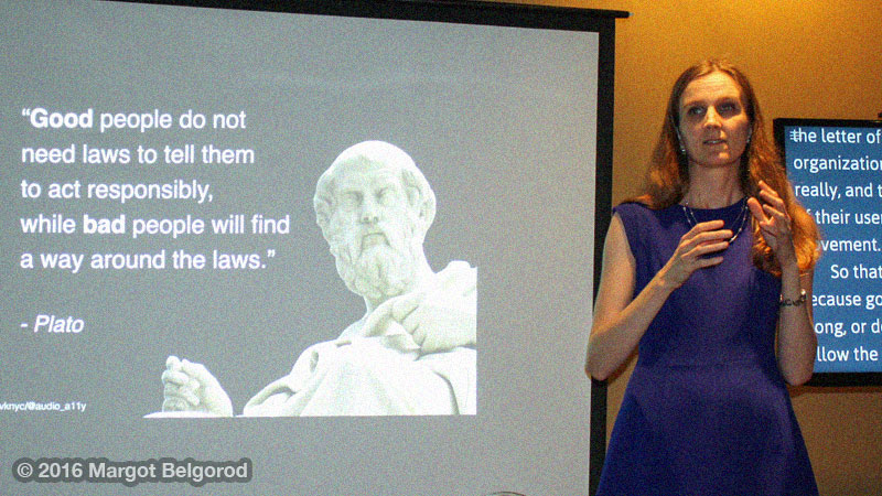 Svetlana in a blue dress standing between a screen with live captions and a screen with a slide showing Plato's quote.