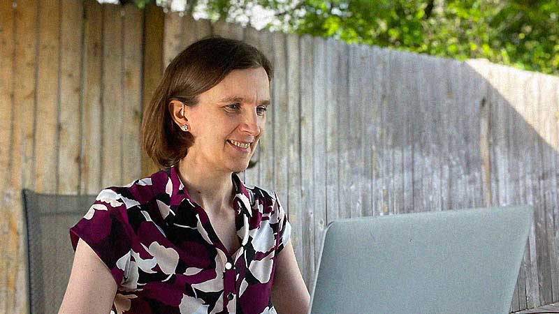 A brunette sitting at a table and smiling at a laptop.